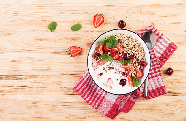 Desayuno saludable - granola, fresas, cerezas, nueces y yogurt en un recipiente sobre una mesa de madera. Concepto de comida vegetariana. Vista superior