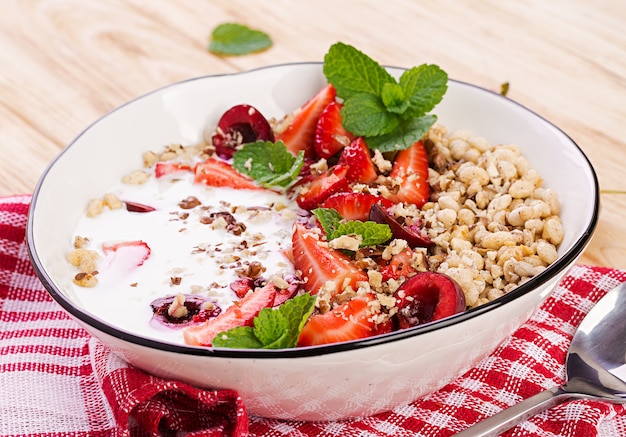 Desayuno saludable - granola, fresas, cerezas, nueces y yogurt en un recipiente sobre una mesa de madera. Concepto de comida vegetariana.