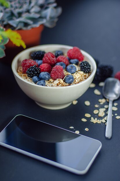 Desayuno saludable. Plato blanco con avena esparcida y diferentes bayas sobre un fondo azul.