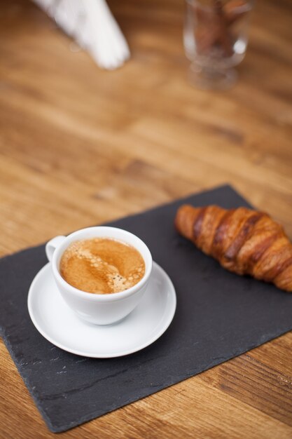 Desayuno con taza de café espresso caliente y croissant en una placa de piedra negra. Aroma de café.