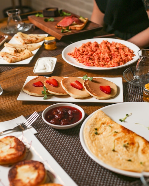 Desayuno con tortitas, crepes, mermelada, tortilla y huevos con tomate