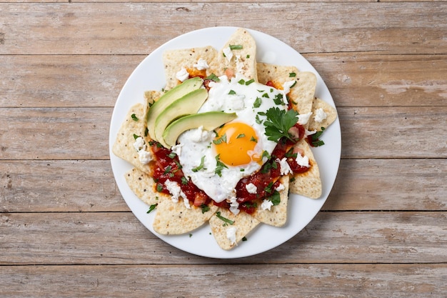 Foto gratuita desayuno tradicional mexicano chilaquiles rojos con huevo en mesa de madera