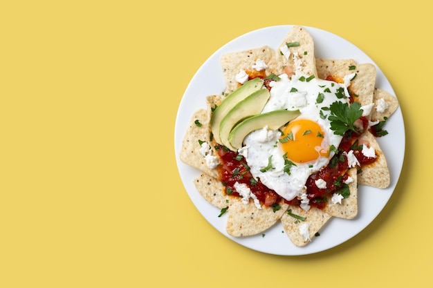 Foto gratuita desayuno tradicional mexicano chilaquiles rojos con huevo sobre fondo amarillo