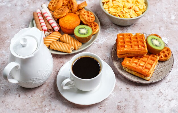 Desayuno con varios dulces, obleas, copos de maíz y una taza de café, vista superior