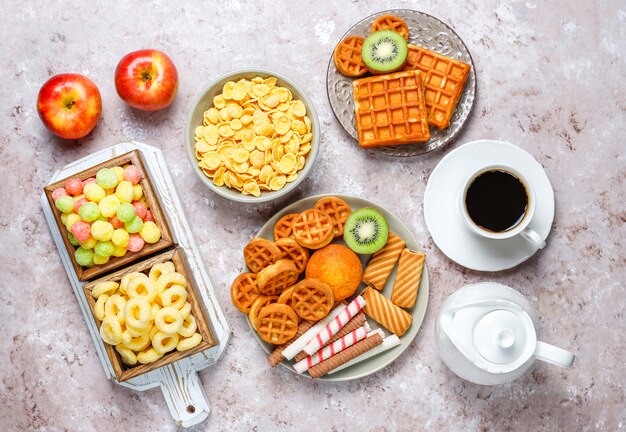 Desayuno con varios dulces, obleas, hojuelas de maíz y una taza de café.