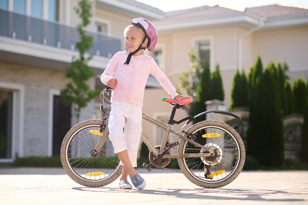 Descansando. Una niña en casco de pie cerca de la bicicleta.