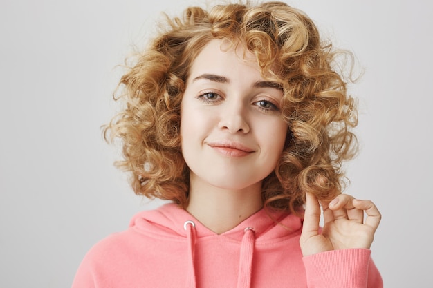 Descarada bastante chica de pelo rizado que parece complacida, sonriendo