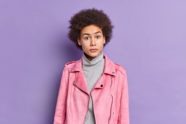 Desconcertado joven y bella mujer afroamericana en chaqueta rosa de moda reacciona sobre algo con expresión insatisfecha