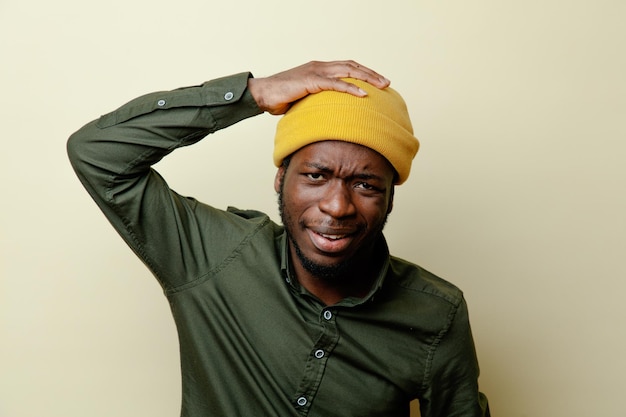 Descontento agarró la cabeza joven afroamericano con sombrero con camisa verde aislada sobre fondo blanco