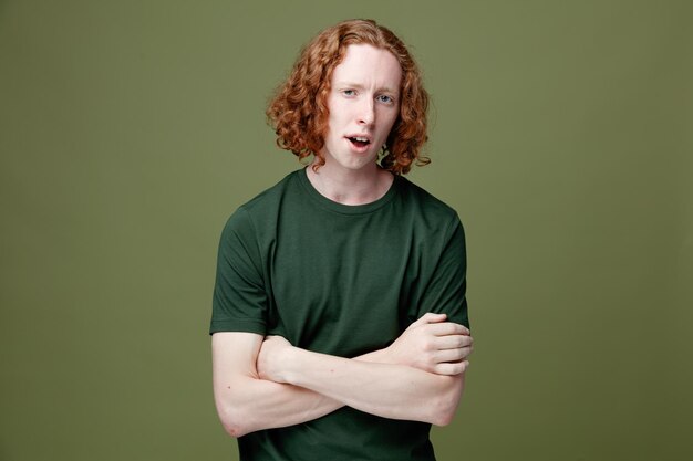 Descontento cruzando las manos joven guapo con camiseta verde aislado sobre fondo verde