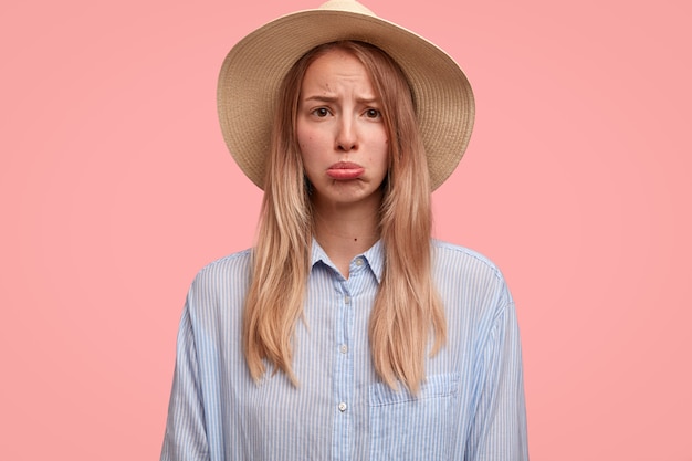 Descontento, encantadora turista con sombrero elegante, bolso con el labio inferior, se siente sola o abusada, no tiene compañero para viajar