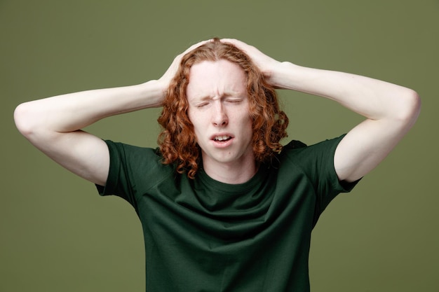 Descontento con los ojos cerrados, agarró la cabeza de un joven apuesto que vestía una camiseta verde aislada de fondo verde