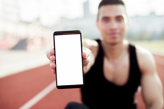 Desenfocado atleta masculino joven que muestra la pantalla del teléfono móvil hacia la cámara