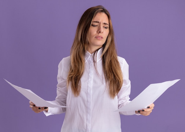 Foto gratuita desorientada joven bastante caucásica sostiene y mira hojas de papel