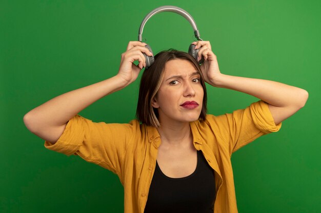 Desorientada mujer bastante caucásica sostiene auriculares sobre la cabeza en verde