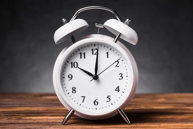 Despertador blanco en mesa de madera con textura que muestra el reloj 10 &#39;