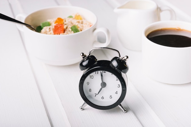 Despertador y desayuno de avena en la mesa blanca