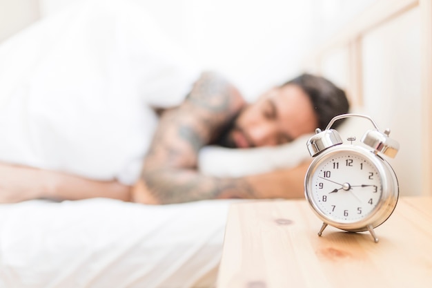 Despertador en el escritorio de madera con hombre durmiendo en el fondo