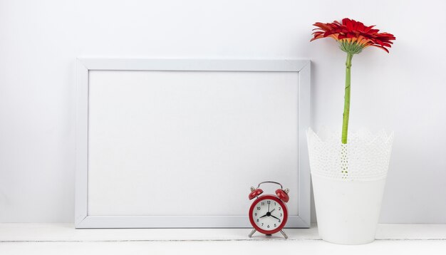 Despertador y flor de gerbera con marco vacío en escritorio