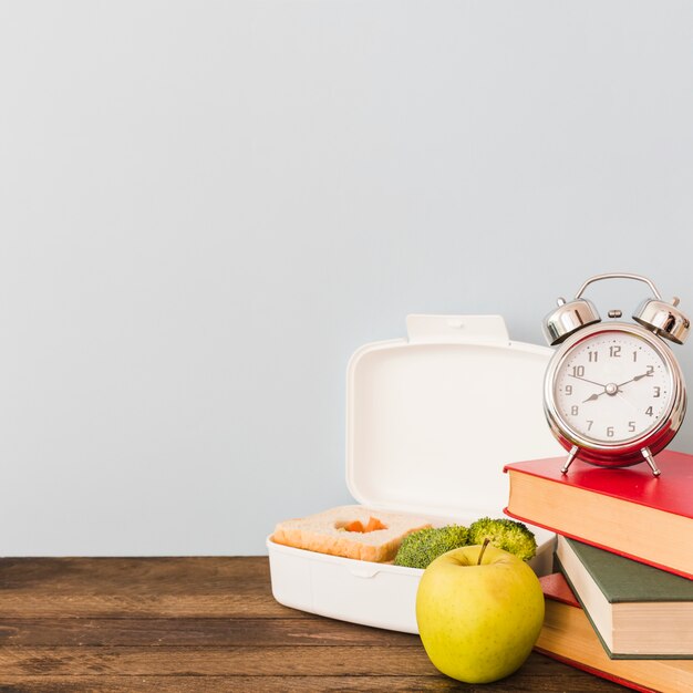 Despertador y libros cerca de comida saludable