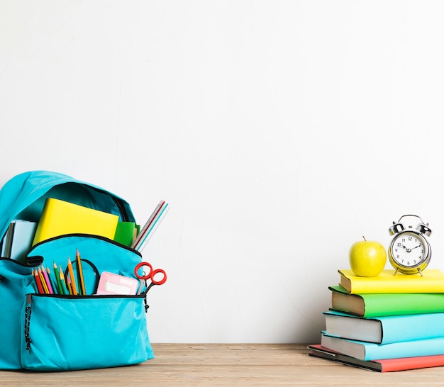 Despertador en la pila de libros y mochila escolar bien equipada con suministros