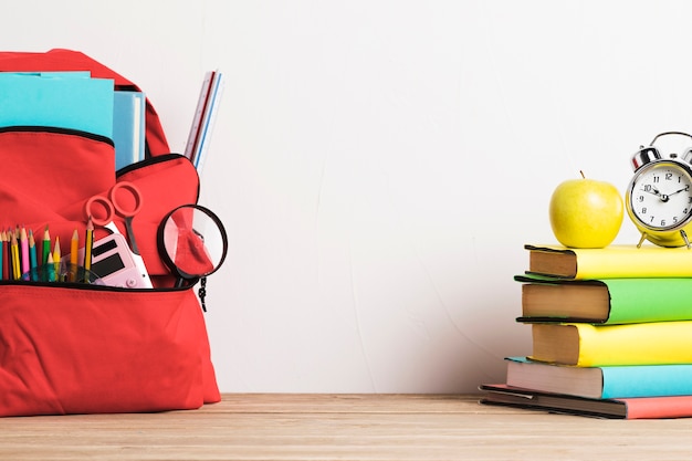 Despertador en la pila de libros y mochila escolar bien equipada con suministros