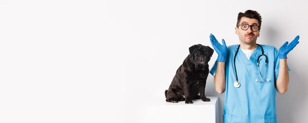 Foto gratuita despistado médico veterinario en matorrales encogiéndose de hombros mirando a la cámara confundido mientras el perro sentado en exa