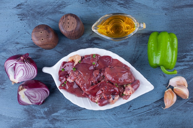 Foto gratuita despojos de pollo en una fuente, cuenco de aceite, sal cebolla, ajo y pimienta sobre la superficie azul