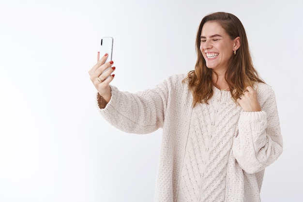 Despreocupada atractiva encantadora carismática mujer europea riendo a carcajadas haciendo videollamada extender el brazo del teléfono inteligente cerrar los ojos riendo alegremente hablando comunicarse en línea a través de internet