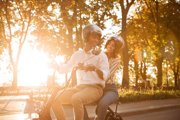 Despreocupada pareja africana monta en moto moderna en el parque y mirándose