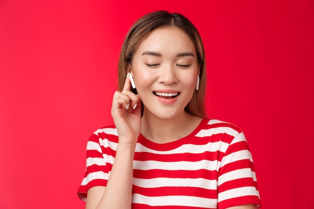 Despreocupado encantado asiático suave mujer cerrar ojos satisfacción sonriendo ampliamente usar auriculares inalámbricos ...