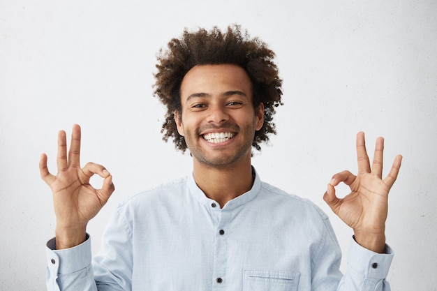 Despreocupado feliz joven afroamericano con peinado funky mostrando el signo de Ok