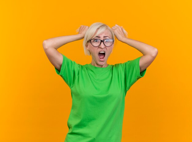 Destacó la mujer eslava rubia de mediana edad con gafas mirando al lado tirando del cabello y gritando aislado sobre fondo amarillo