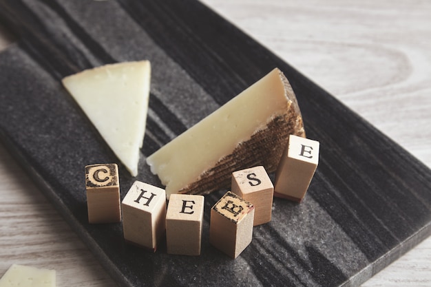 Detalle de cerca de ladrillo de letra de madera enfocada cerca de queso de cabra desenfocado aislado en tablero de piedra de mármol sobre mesa de madera blanca