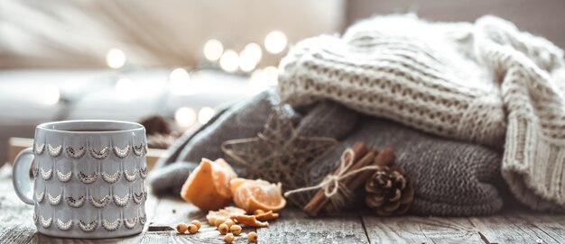 Detalles de naturaleza muerta en la sala de estar interior de la casa. Hermosa taza de té con mandarinas y suéteres sobre fondo de madera. Acogedor concepto otoño-invierno