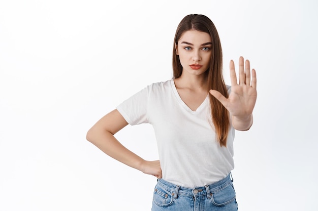 Foto gratuita detente, quédate atrás. chica seria y segura estirar la mano para decir no, prohibir, mantener el distanciamiento social en caso de pandemia, hacer un gesto de bloqueo, rechazar o prohibir algo, fondo blanco.