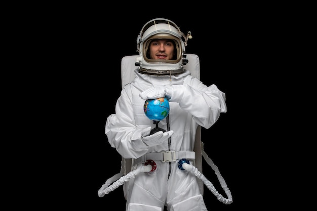 Día del astronauta astronauta en traje espacial blanco sonriendo casco de vidrio abierto sosteniendo y girando globo terráqueo