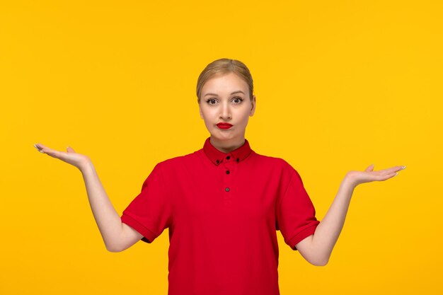 Día de la camisa roja chica confundida agitando las manos en el aire con una camisa roja sobre un fondo amarillo