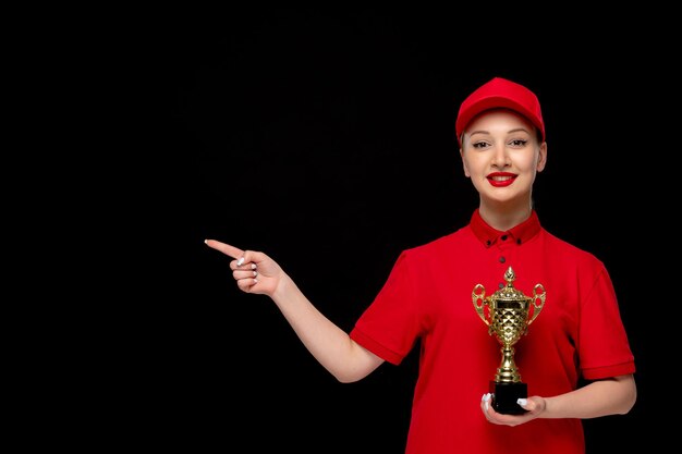 Día de la camisa roja dama bonita sosteniendo un trofeo en una gorra roja con camisa y lápiz labial brillante