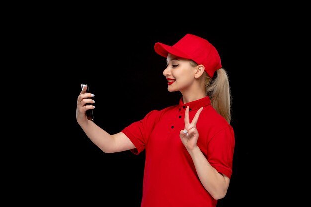 Día de la camisa roja niña encantadora sonriendo y hablando selfie en gorra roja con camisa y lápiz labial brillante