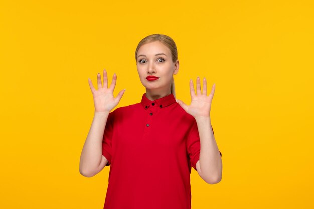 El día de la camisa roja sorprendió a la chica con las manos arriba en una camisa roja sobre un fondo amarillo