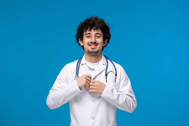 Día del doctor chico lindo guapo rizado en uniforme médico abotonándose una camisa