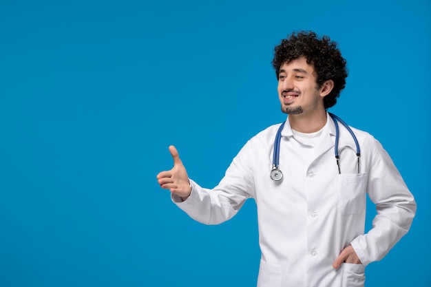 Día del doctor chico lindo guapo rizado en uniforme médico dando gesto de apretón de manos