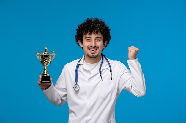 Día del doctor chico lindo guapo rizado en uniforme médico emocionado por un premio de oro