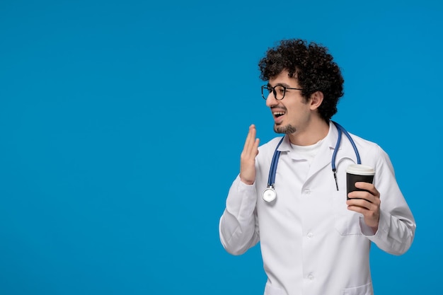 Día del doctor chico lindo guapo rizado en uniforme médico con gafas con papercup