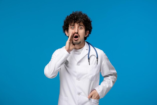 Día del doctor chico lindo guapo rizado en uniforme médico llamando a alguien con las manos en la cara