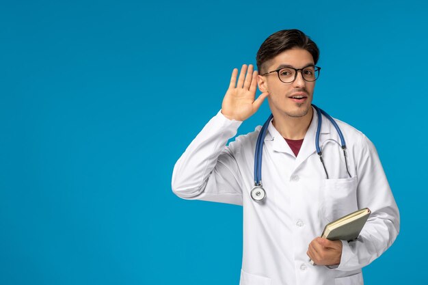 Día del doctor lindo joven apuesto en bata de laboratorio y gafas escuchando a escondidas y sosteniendo un libro