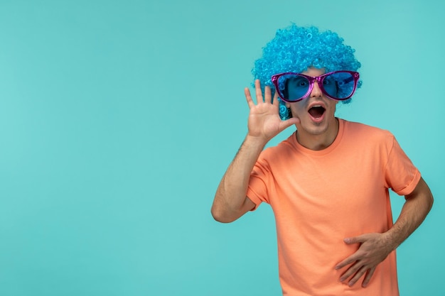 Foto gratuita día de los inocentes chico clownlistening cabello azul rosa gafas de sol grandes mano divertida cerca de la oreja