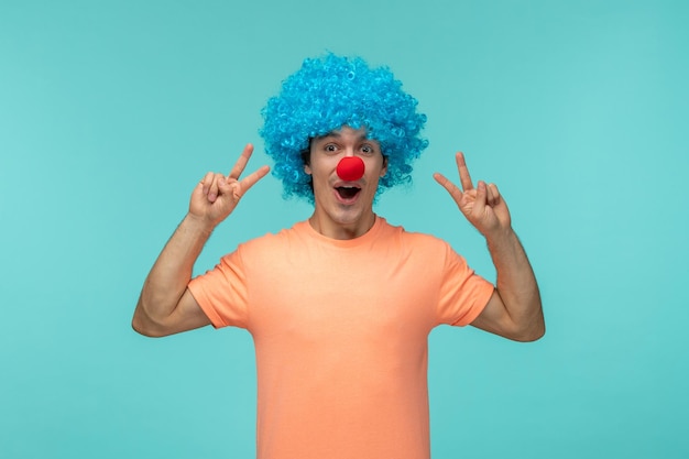 Día de los inocentes chico payaso feliz mostrando el signo de la paz cabello azul emocionado gracioso nariz roja boca abierta