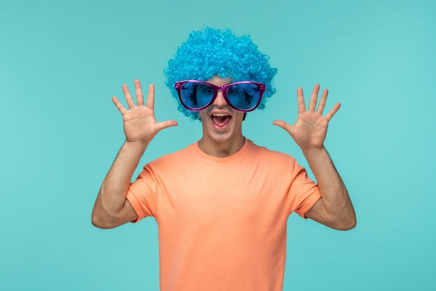 Día de los inocentes chico payaso gritando manos arriba boca abierta cabello azul rosa gafas de sol grandes gritos divertidos